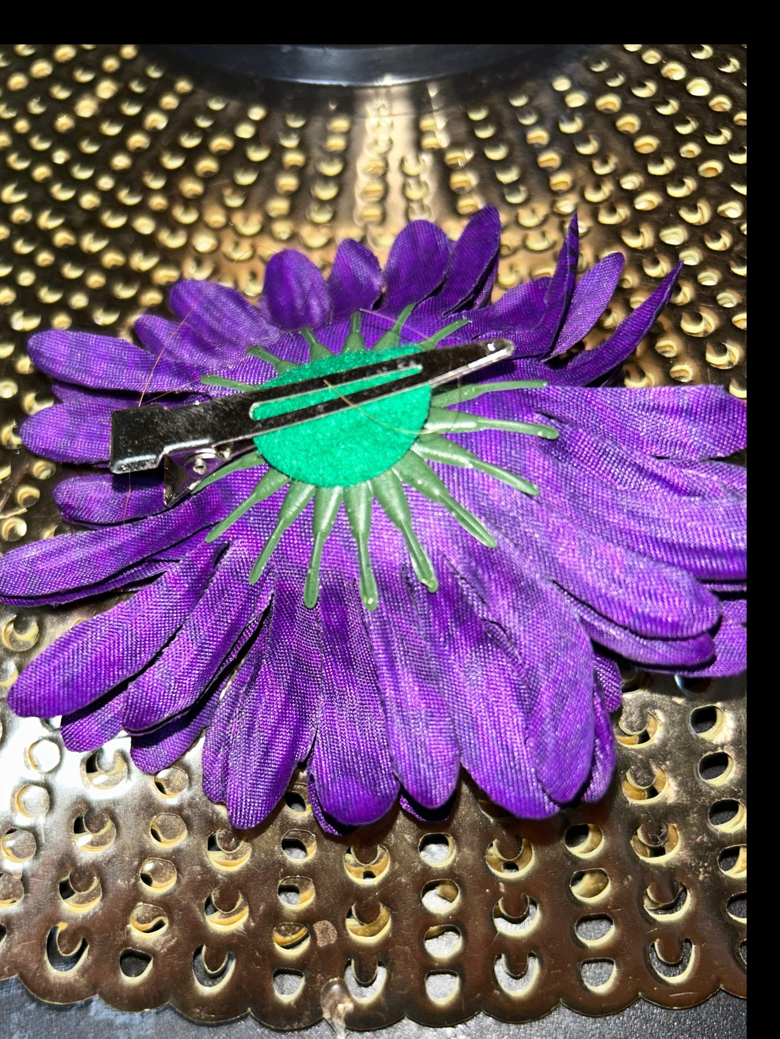 Purple flower-shaped hair clip on a textured metal surface