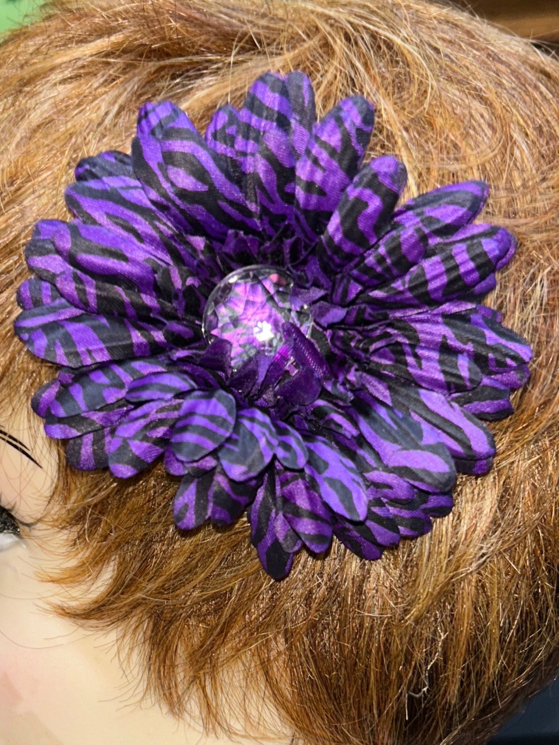 Mannequin head with a purple flower in hair against a blurred indoor background