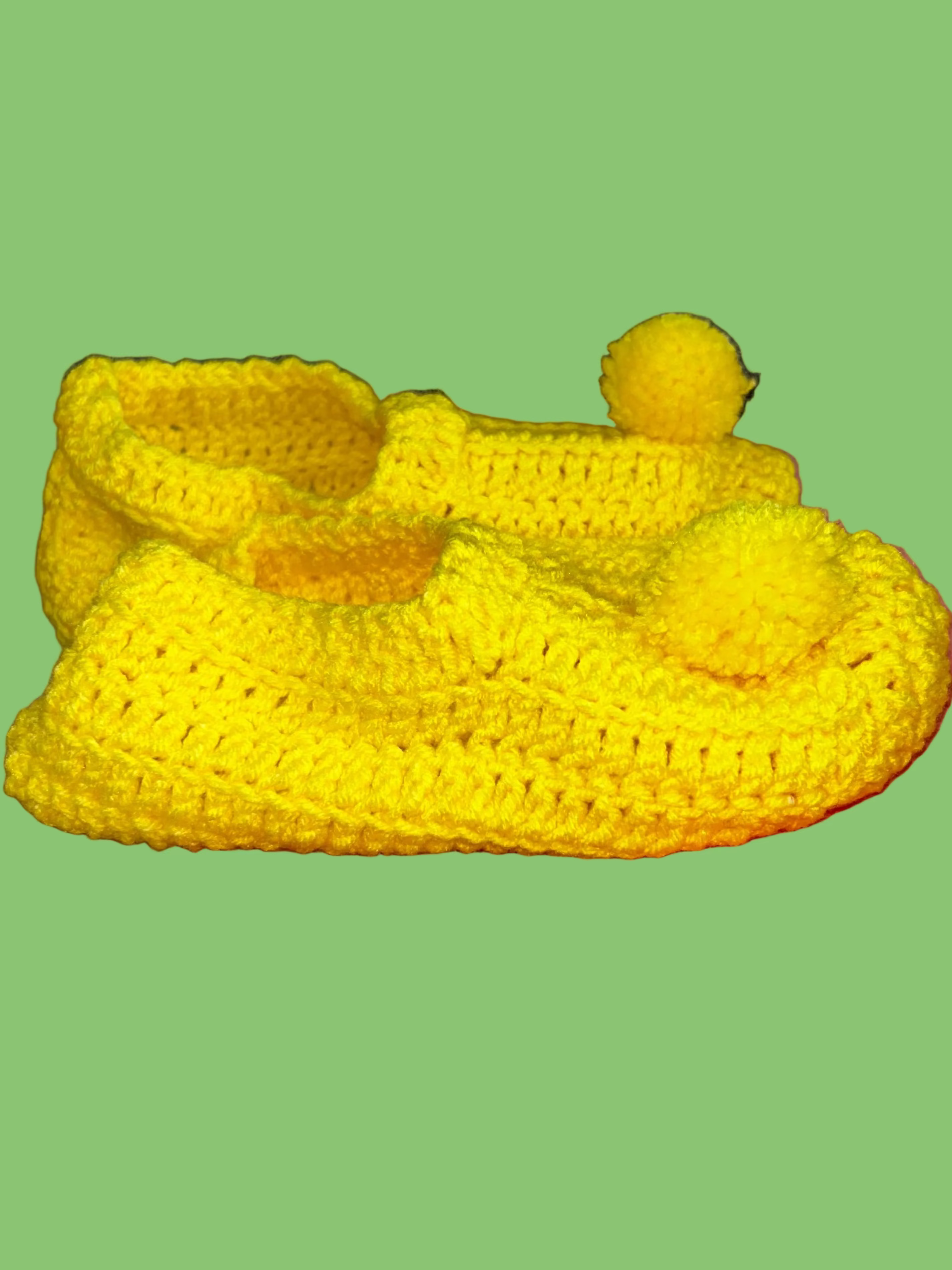 Yellow crocheted bootie shoe with a pom-pom on a  background
