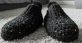 Pair of black textured slippers on a pink and white striped surface