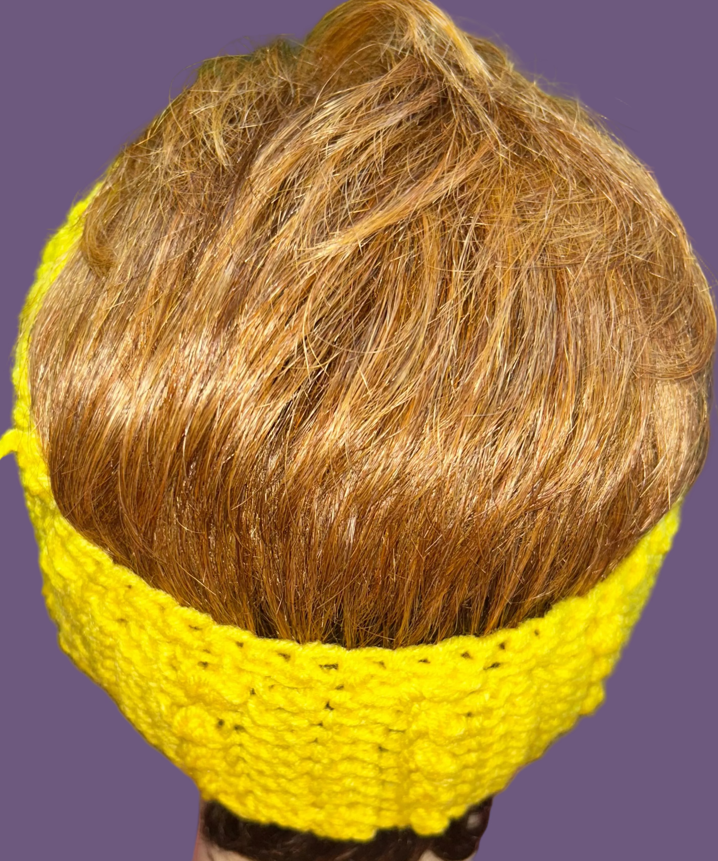 Mannequin head with brown hair wearing a crocheted headband on a pink surface.