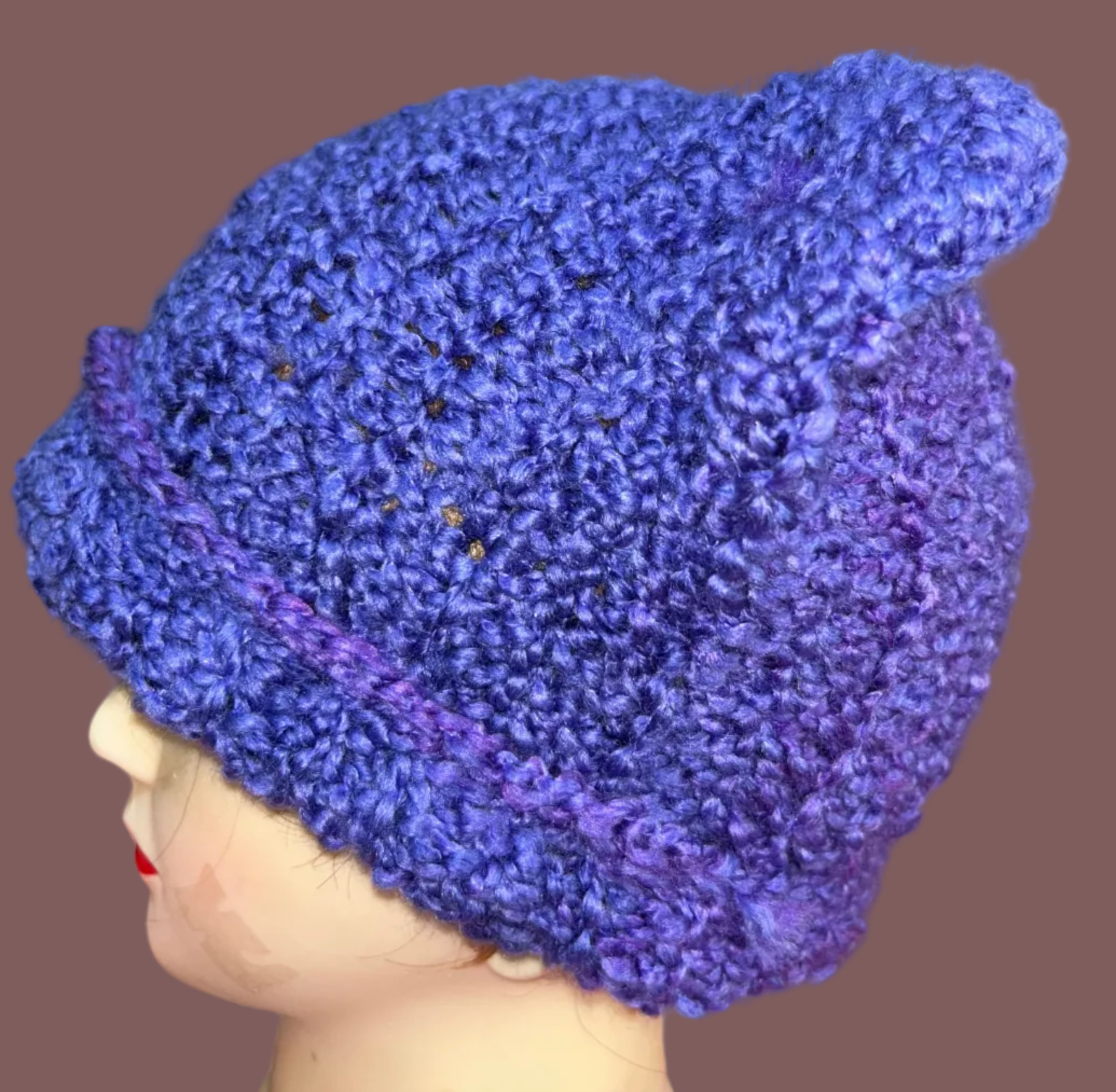Blue knitted hat on a mannequin head with a colorful tapestry in the background
