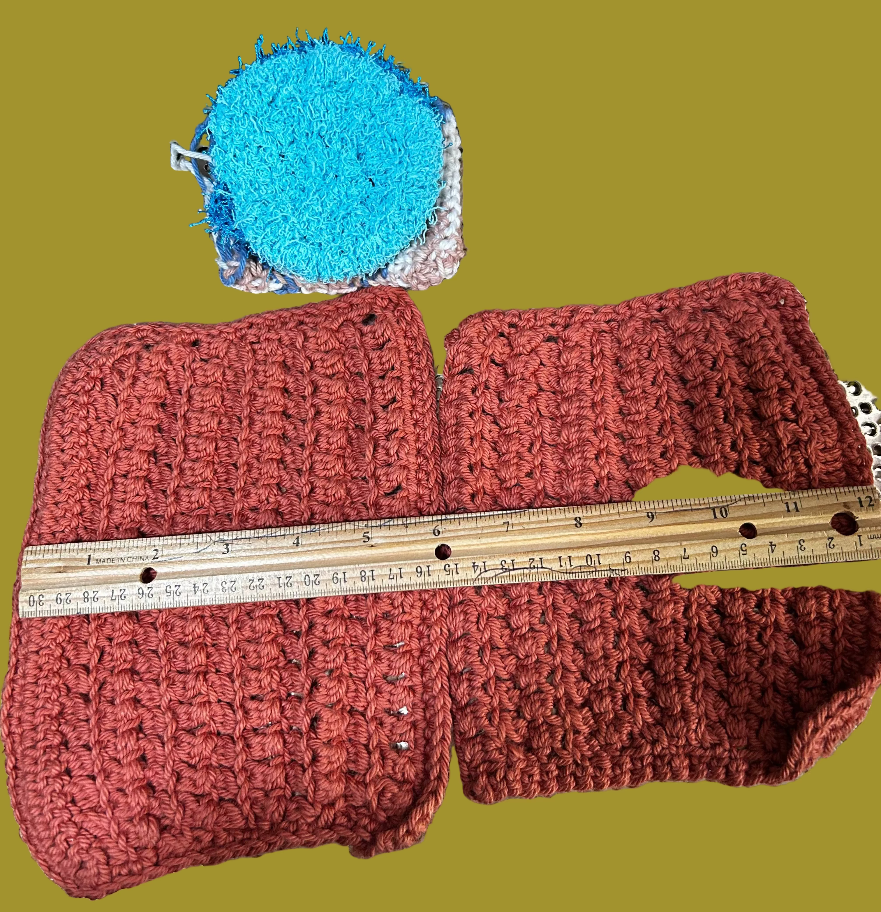 Two crocheted items, one blue and one red, on a textured surface with a ruler for scale.