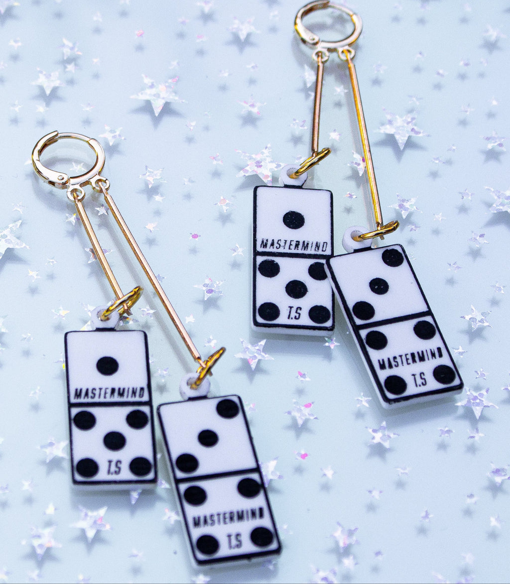 Pair of earrings with domino-like designs on a light blue background with star patterns.
