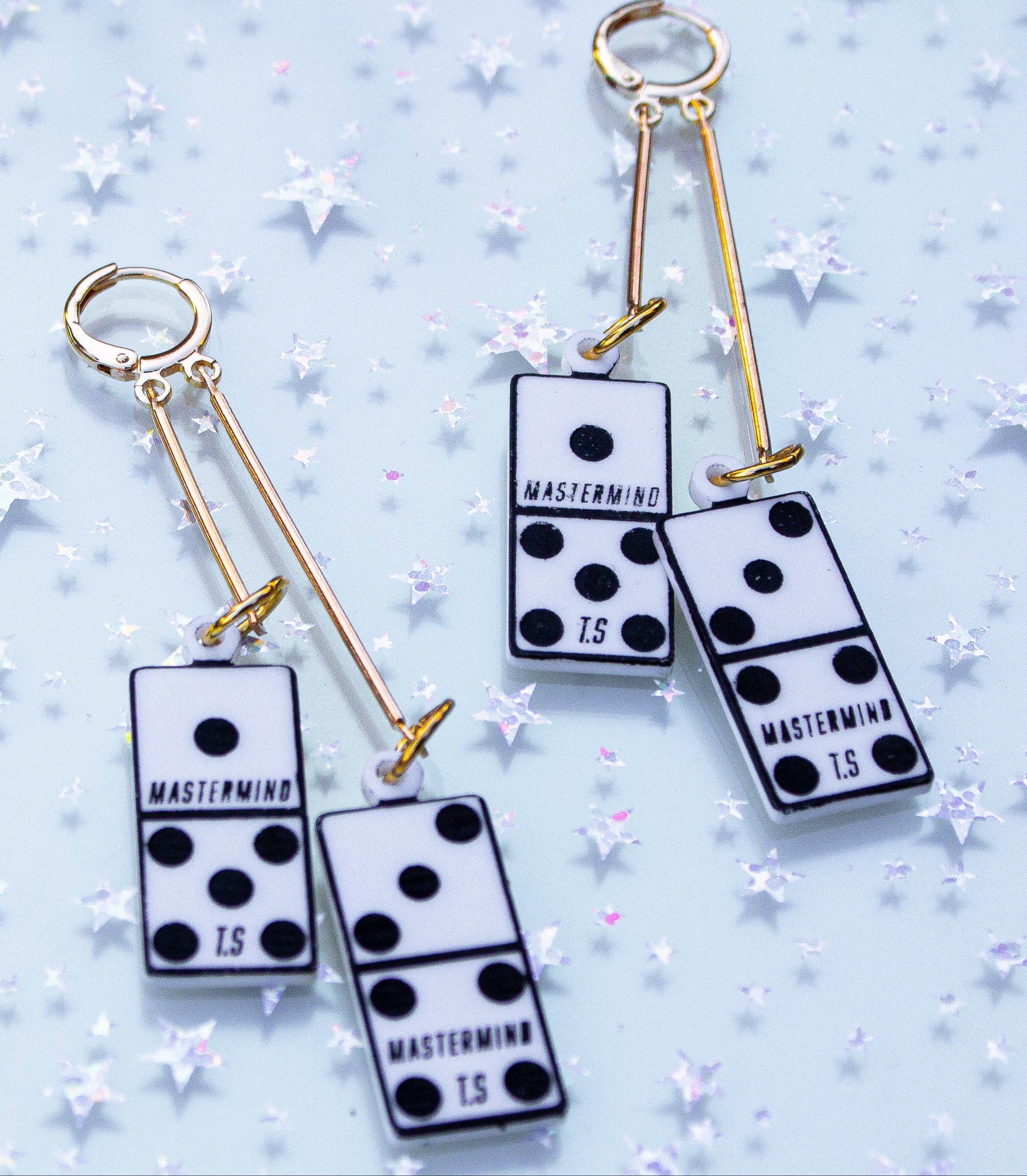 Pair of earrings with domino-like designs on a light blue background with star patterns.
