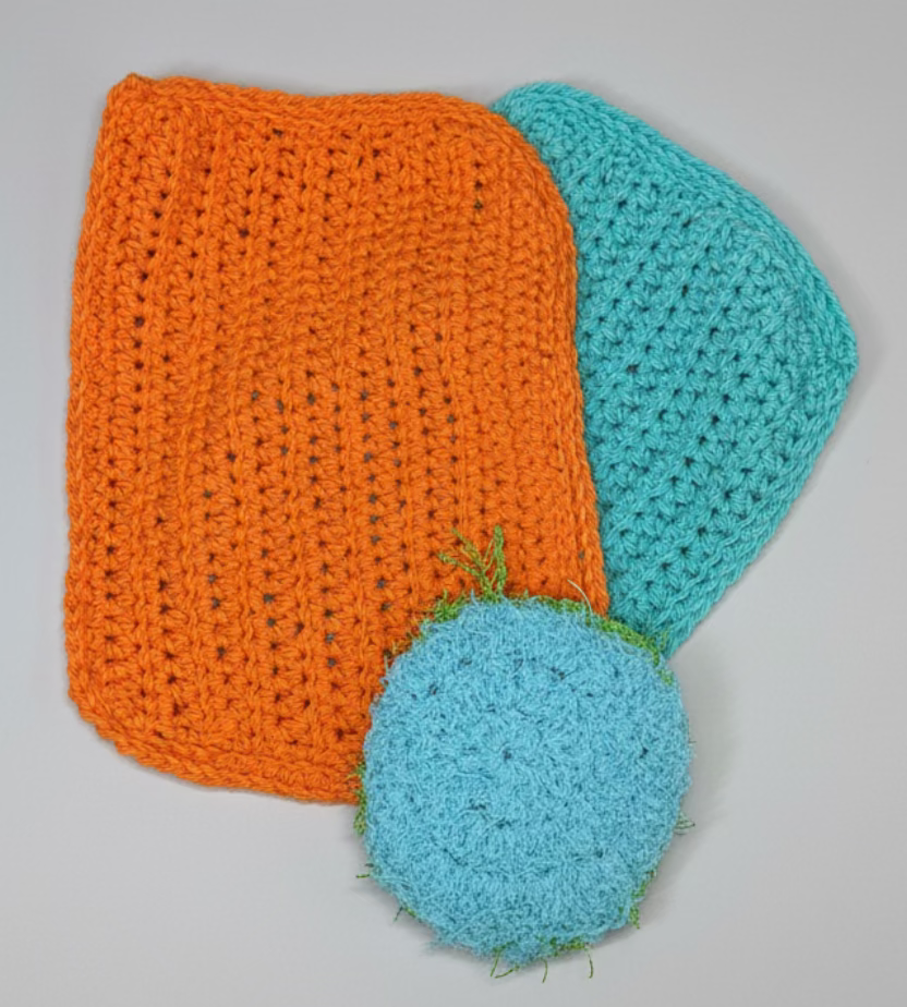 Two crocheted items, one orange and one blue, on a textured metal surface.