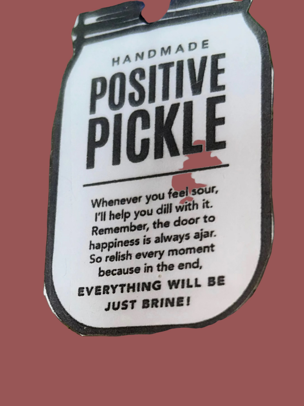 Metallic object with a 'Positive Pickle' label on a textured green surface