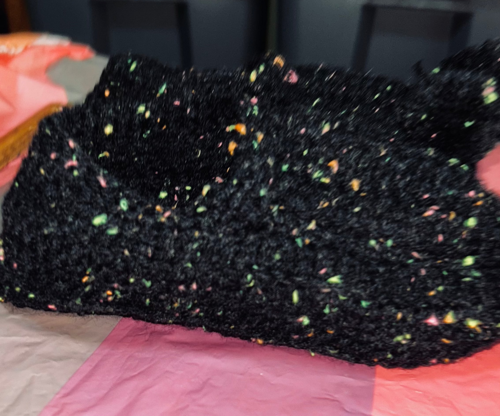 Black textured sponge held by a hand on a pink fabric background