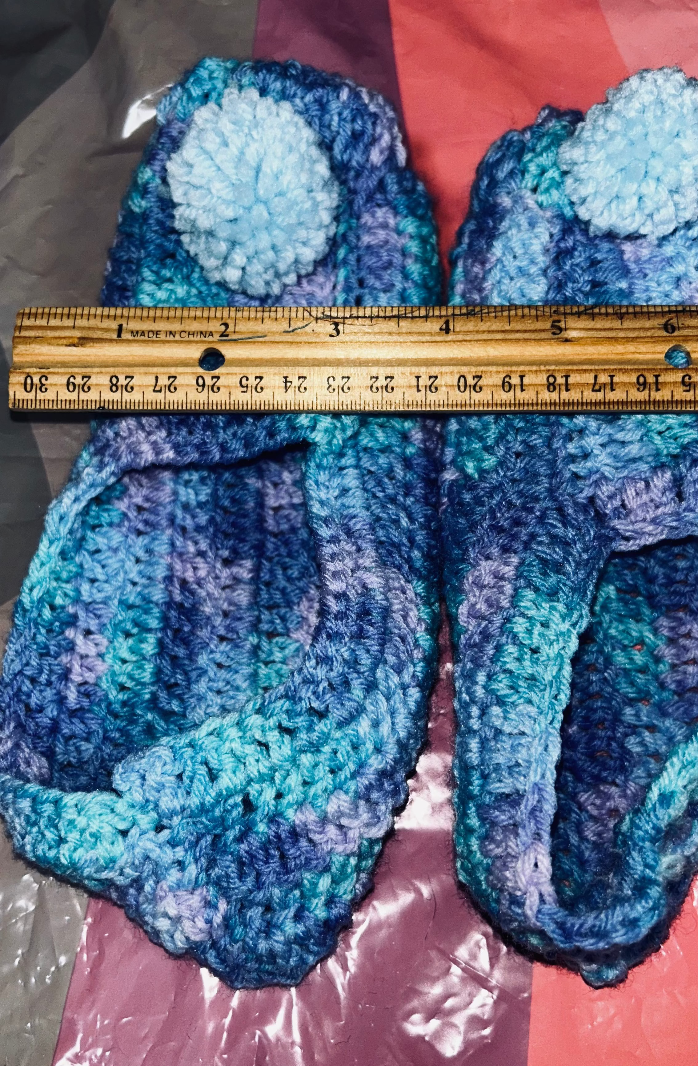 Blue crocheted slippers with a ruler for scale on a multicolored fabric background