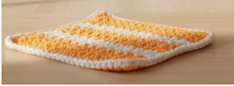 Crocheted orange and white square with a ruler for scale on a colorful background
