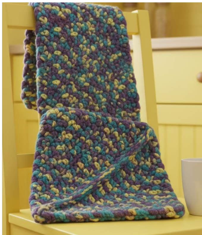 Colorful knitted blanket on a yellow surface with a white mug.