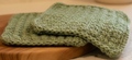 Green knitted dishcloth on a wooden cutting board with a blurred background