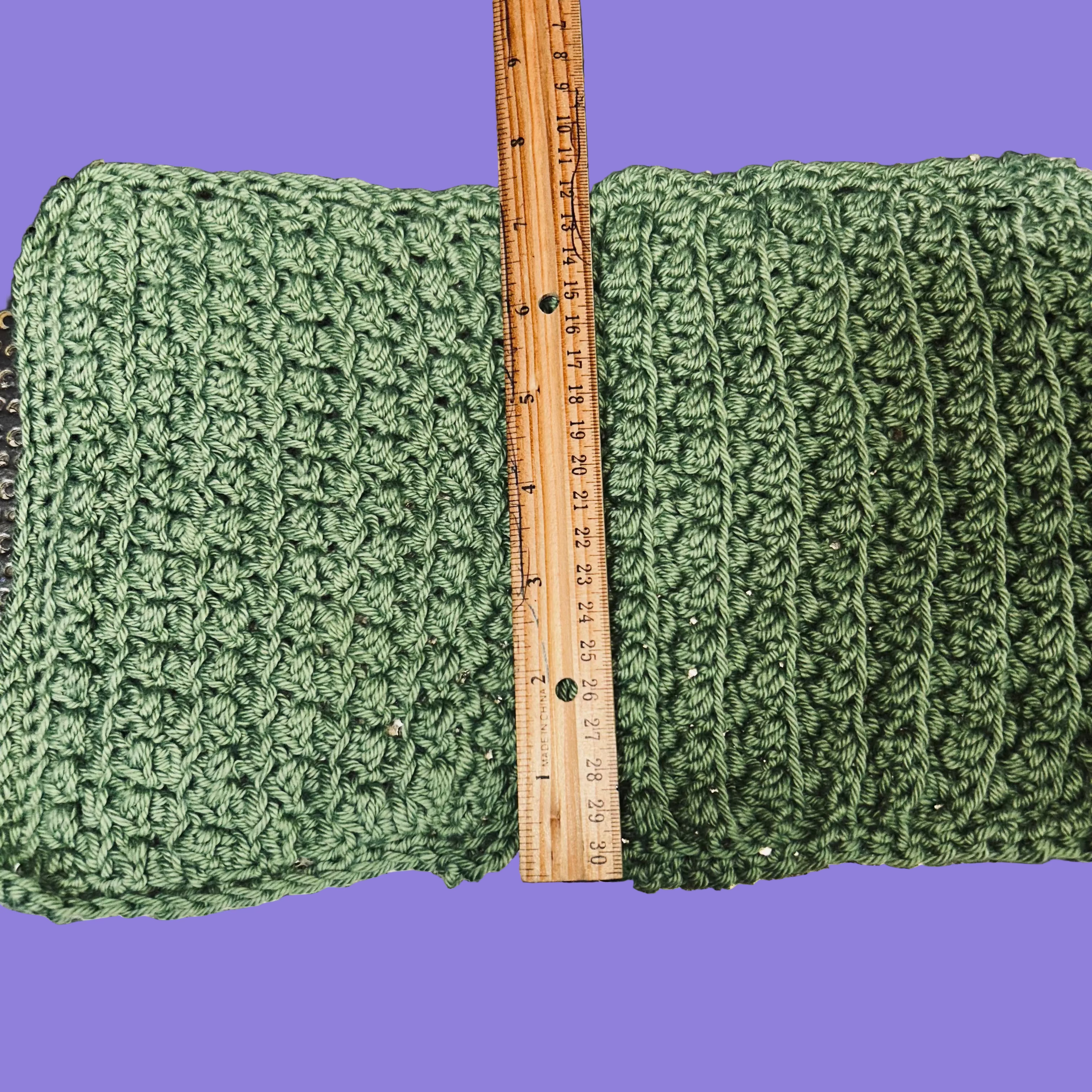 Green crocheted fabric with a wooden ruler for scale on a metallic background