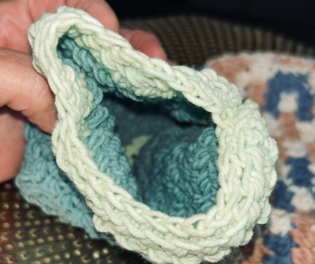 Hand holding a crocheted dishcloth with a textured surface in the background