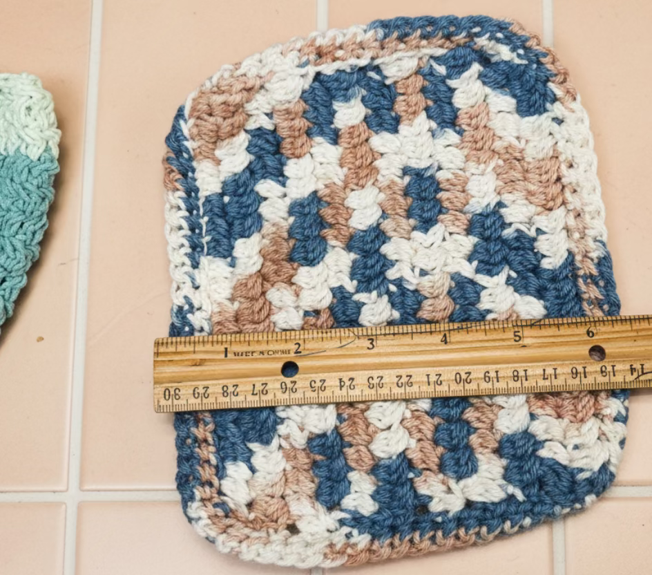 Decorative dish cloth with a geometric pattern on a textured surface, measured by a ruler.