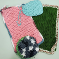 crocheted items including a green pouch, green square, and black & white scrubbie on a textured surface.