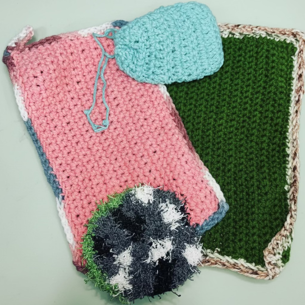 crocheted items including a green pouch, green square, and black & white scrubbie on a textured surface.