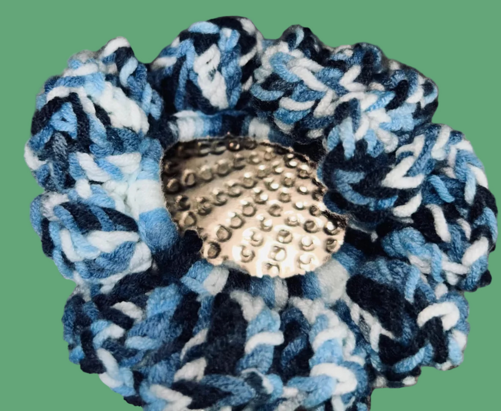Blue and white braided scrunchie with a textured button on a metallic background