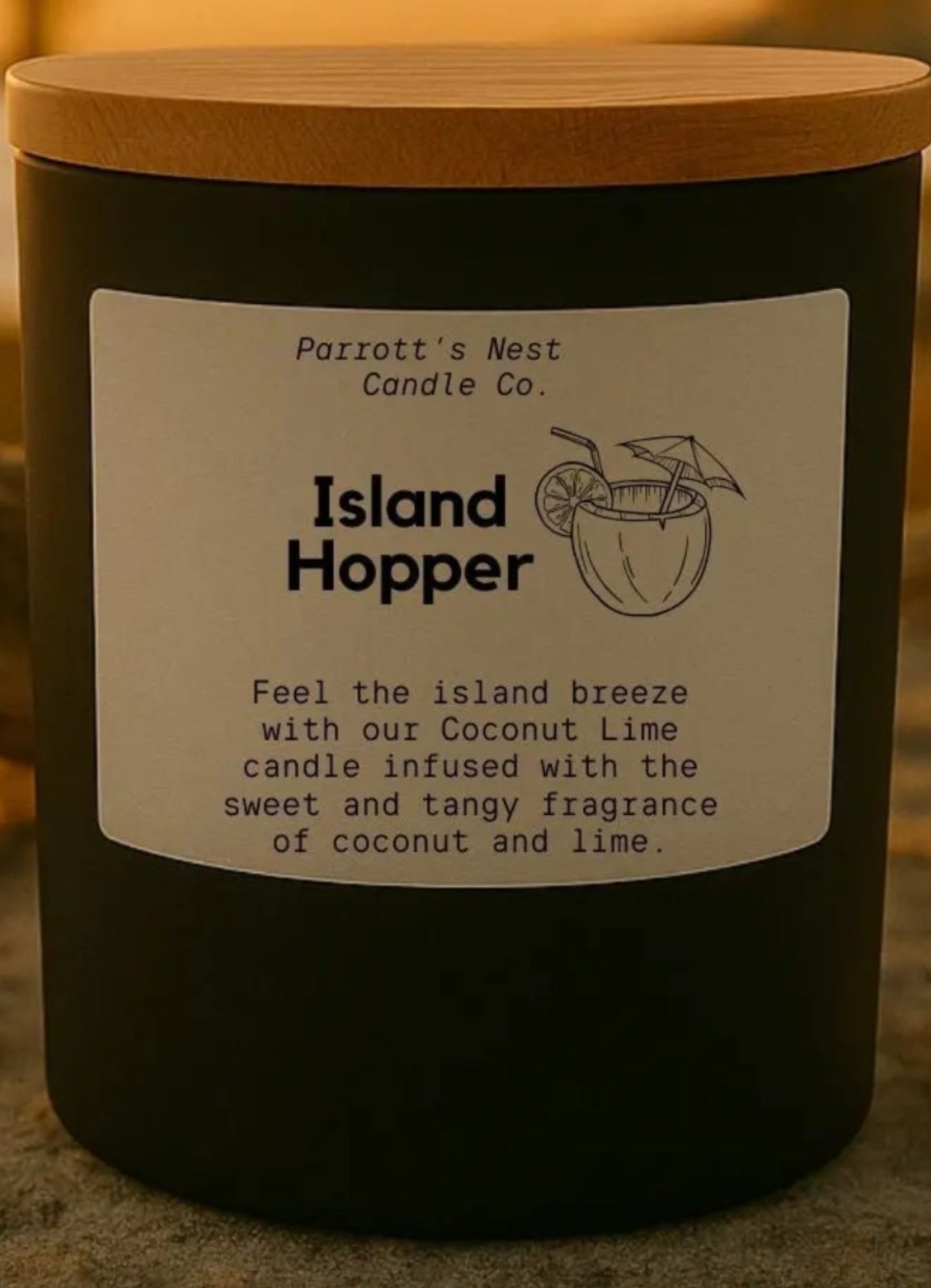 Candle labeled 'Island Hopper' on a sandy surface with shells and a sunset background