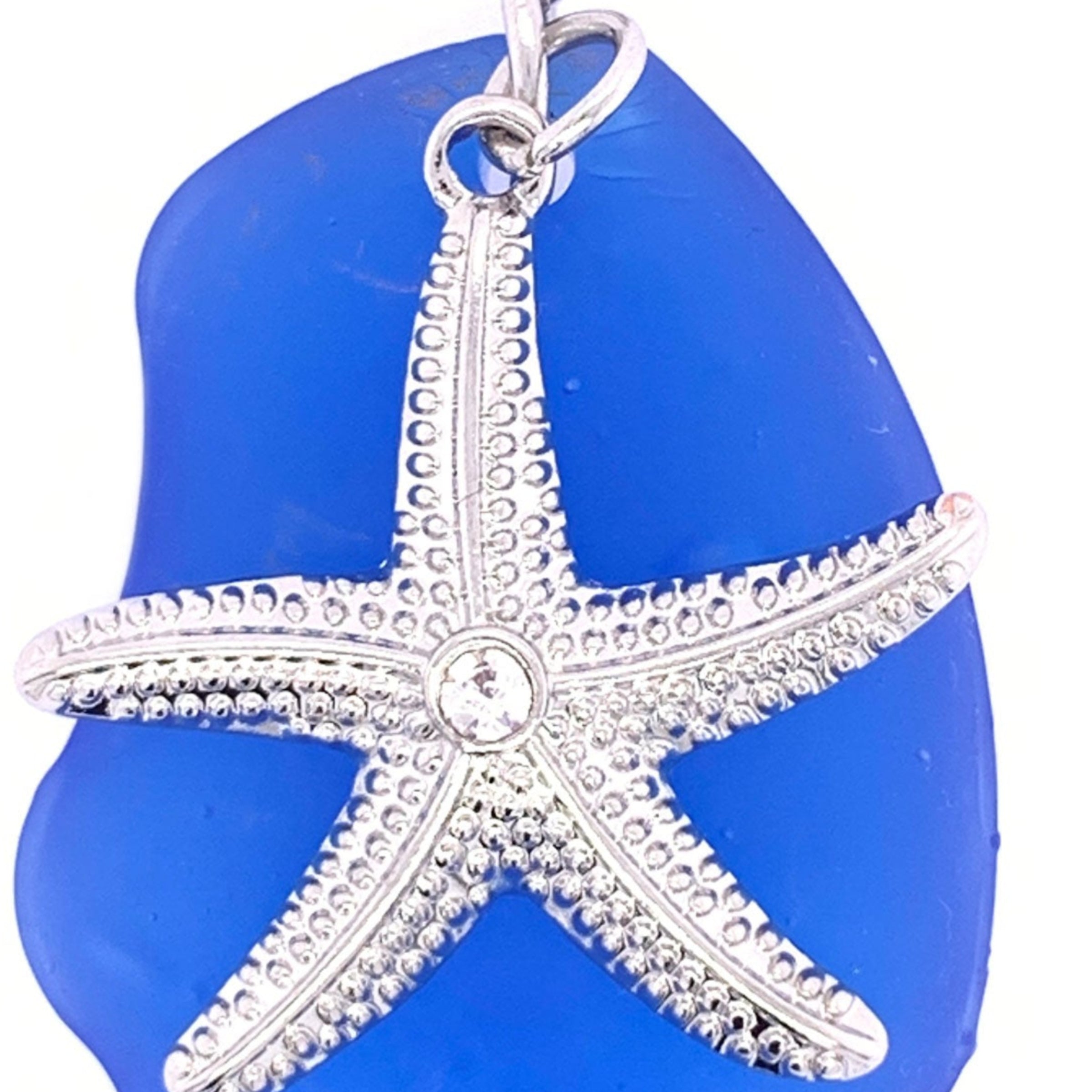 Blue sea glass pendant with a silver starfish charm on a white background