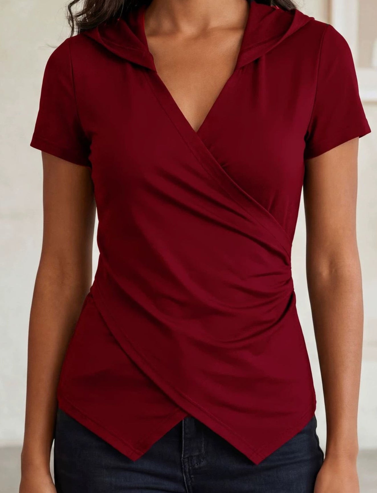 Woman wearing a burgundy top with a draped design in an indoor setting.