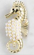 Gold seahorse-shaped brooch with pearl embellishments on a light gray background