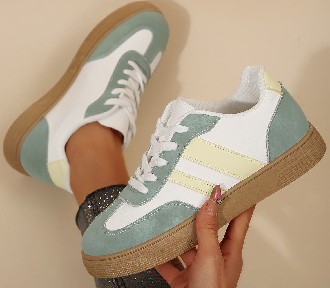 White sneakers with green and yellow accents held by a hand against a beige background