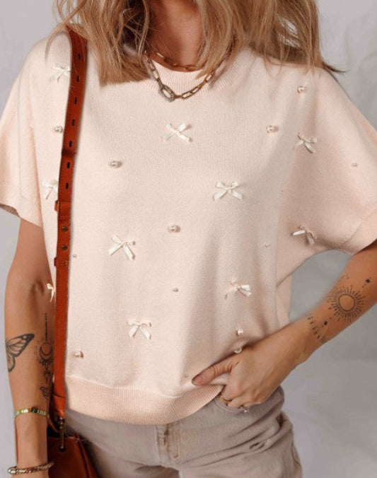 Woman wearing a beige blouse with bow patterns and holding a brown bag.