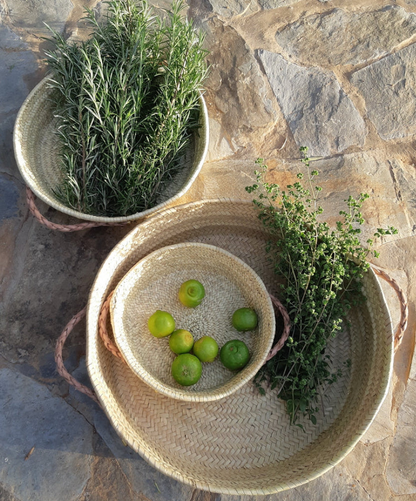 Two woven bowls on a stone surface with green apples and herbs.