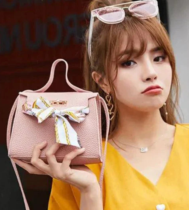 Woman holding a pink handbag with a bow, wearing a yellow top.