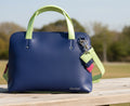 Blue handbag with green handles and strap on a white background