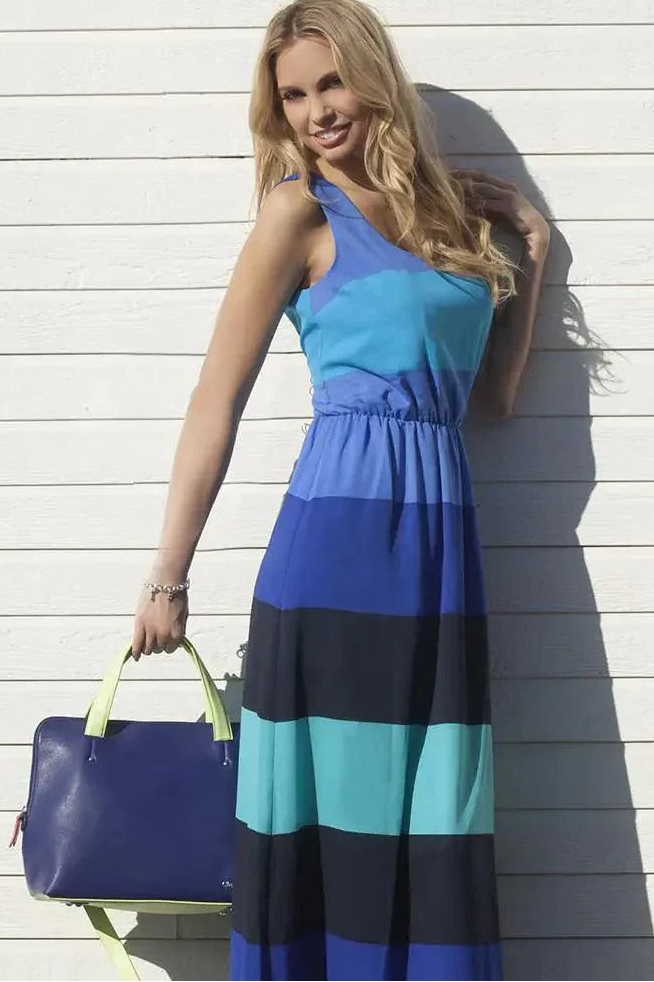 Woman in a blue and black striped dress holding a matching handbag against a light wooden wall.