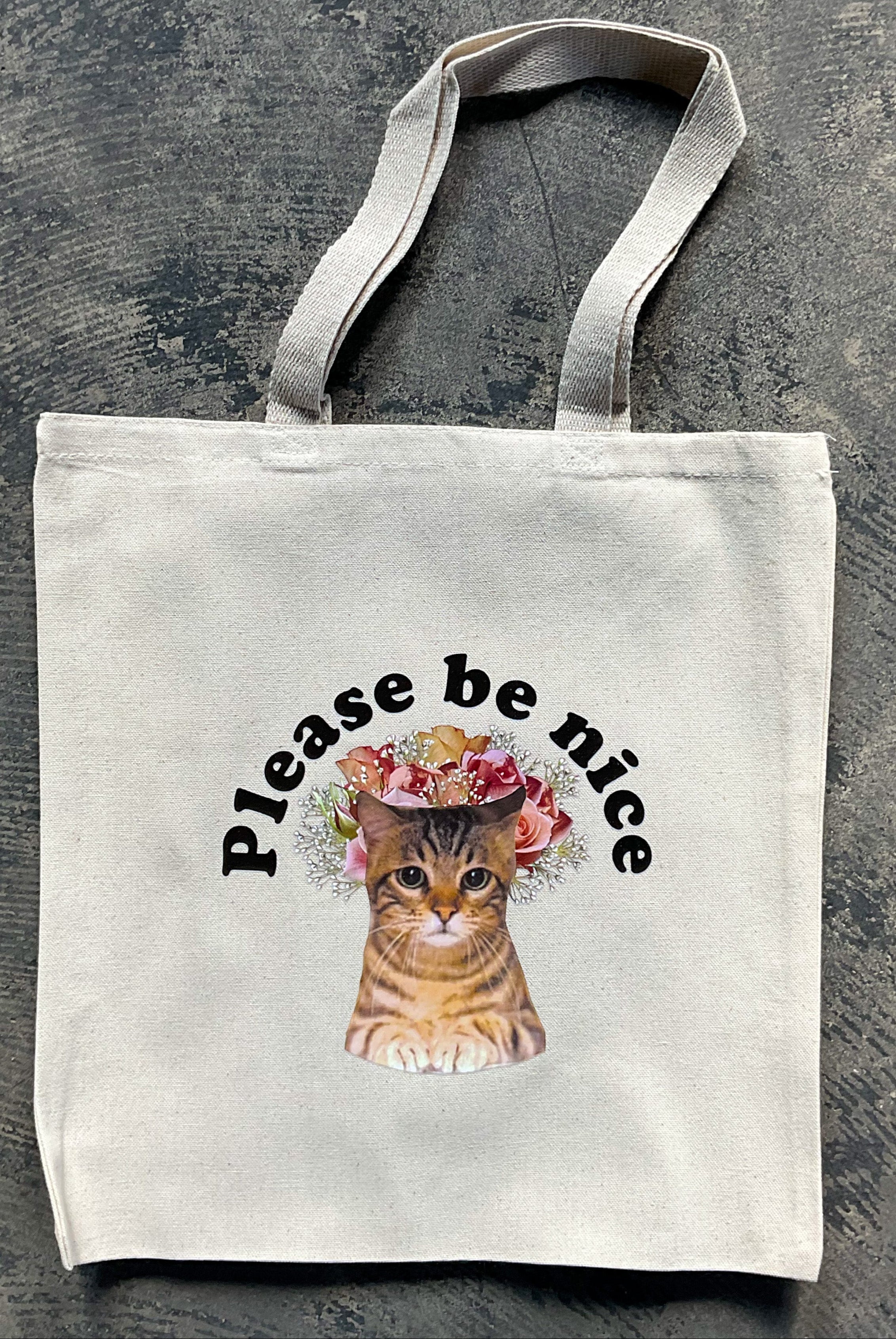 Tote bag with a cat illustration and 'Please be nice' text on a textured surface