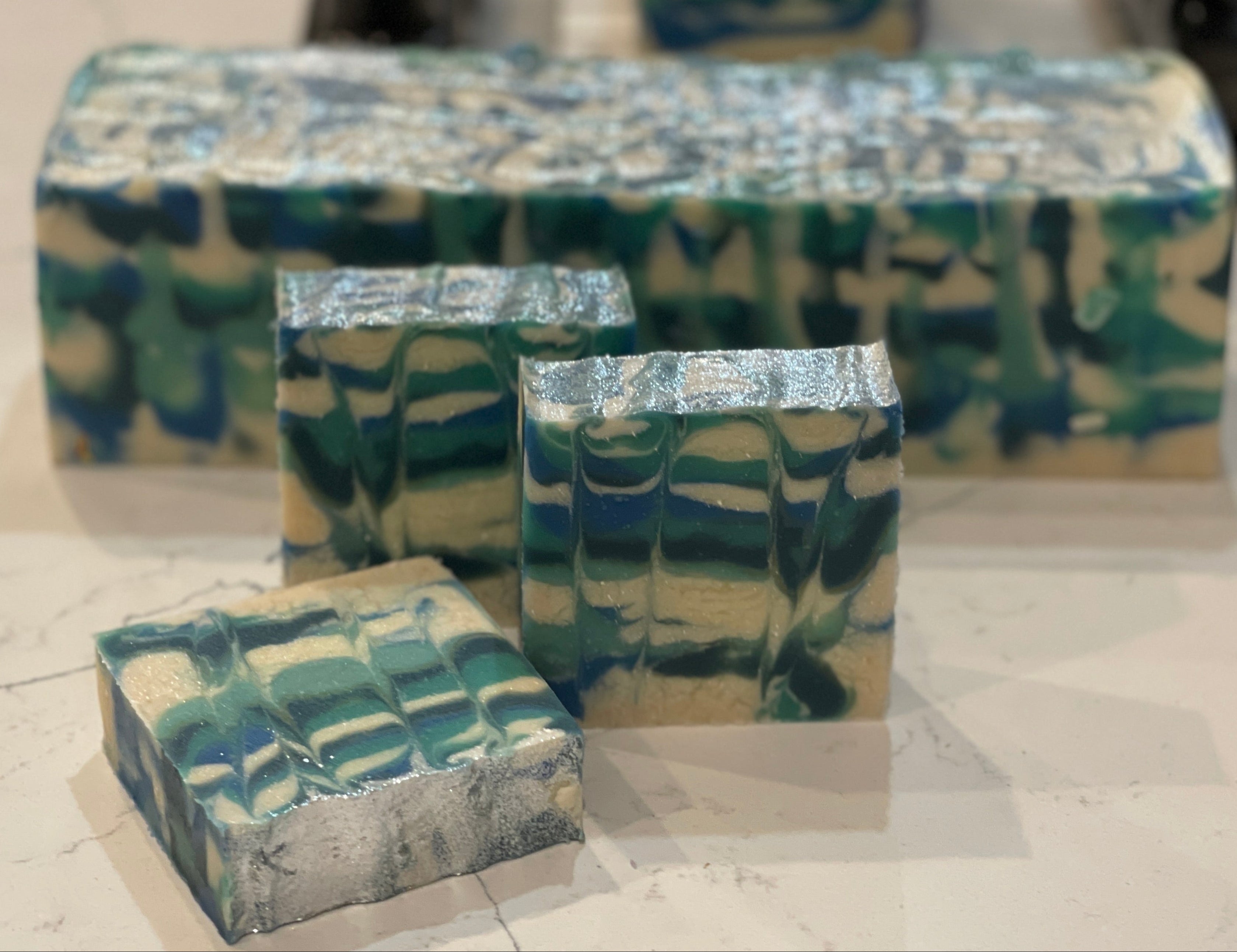 Handmade soap bars with a marbled design in green, blue, and beige on a light surface.
