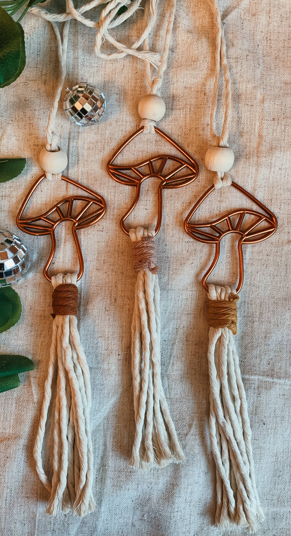 Macrame mushroom decorations with tassels on a textured surface with green leaves.