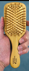 Hand holding a wooden hairbrush against a blue background