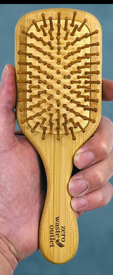 Hand holding a wooden hairbrush against a blue background