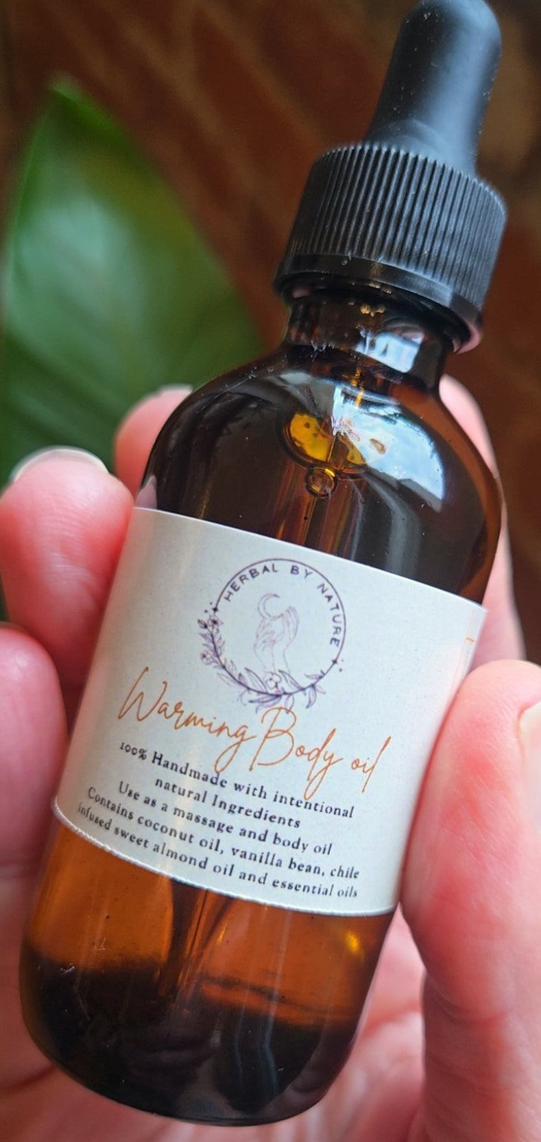 Hand holding a bottle of warming body oil with a label.