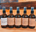 Five bottles of 'Natura by Nature' product on a wooden surface